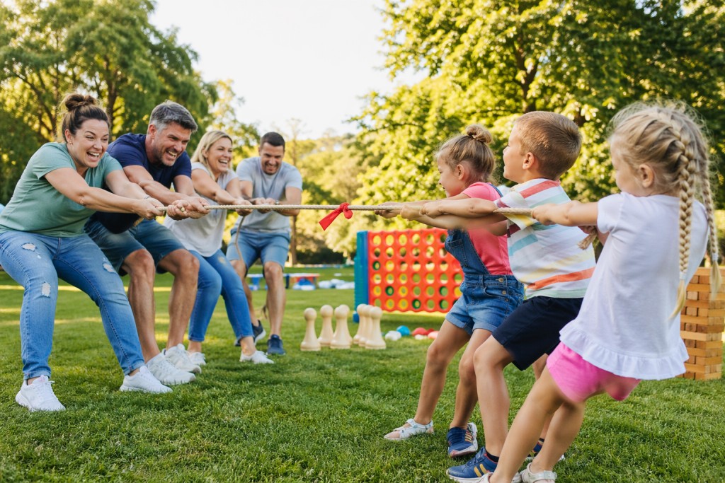 Eine Gruppe Erwachsener tritt gegen eine Kindergruppe beim Tauziehen auf einer grünen Wiese an.